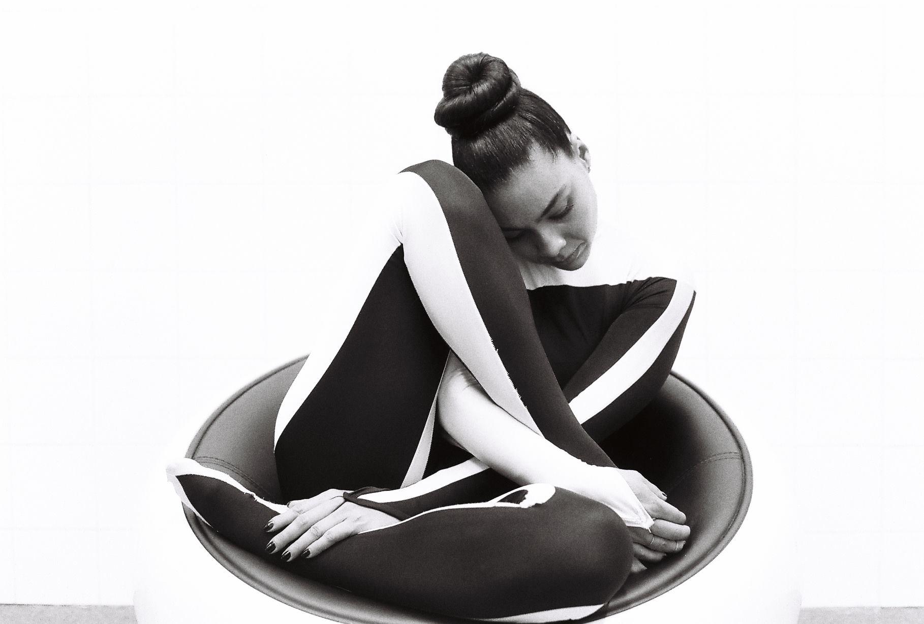 La danseuse pose en costume de scène noir et blanc sur un siège des années 60 pour une photographie argentique.