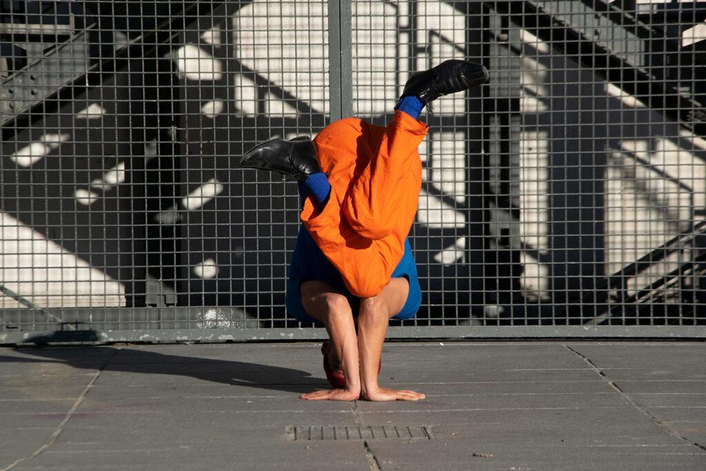 Un bboy fait de la breakdance en tenue orange et bleue sur le parvis de Beaubourg à Paris.