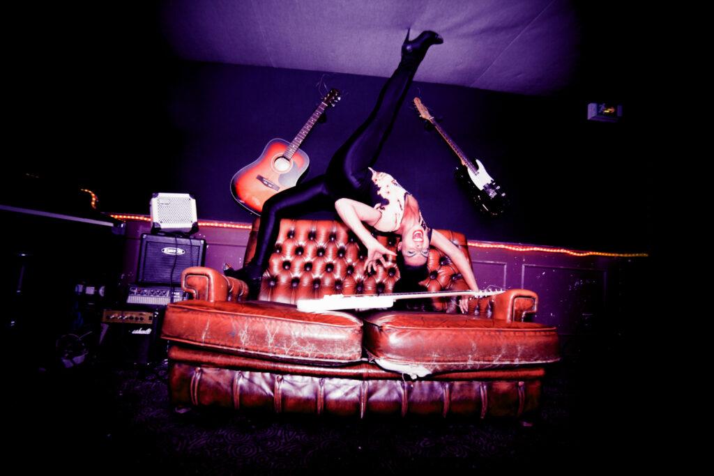 Une contorsionniste fait une posture sur un canapé entouré de guitares rock.